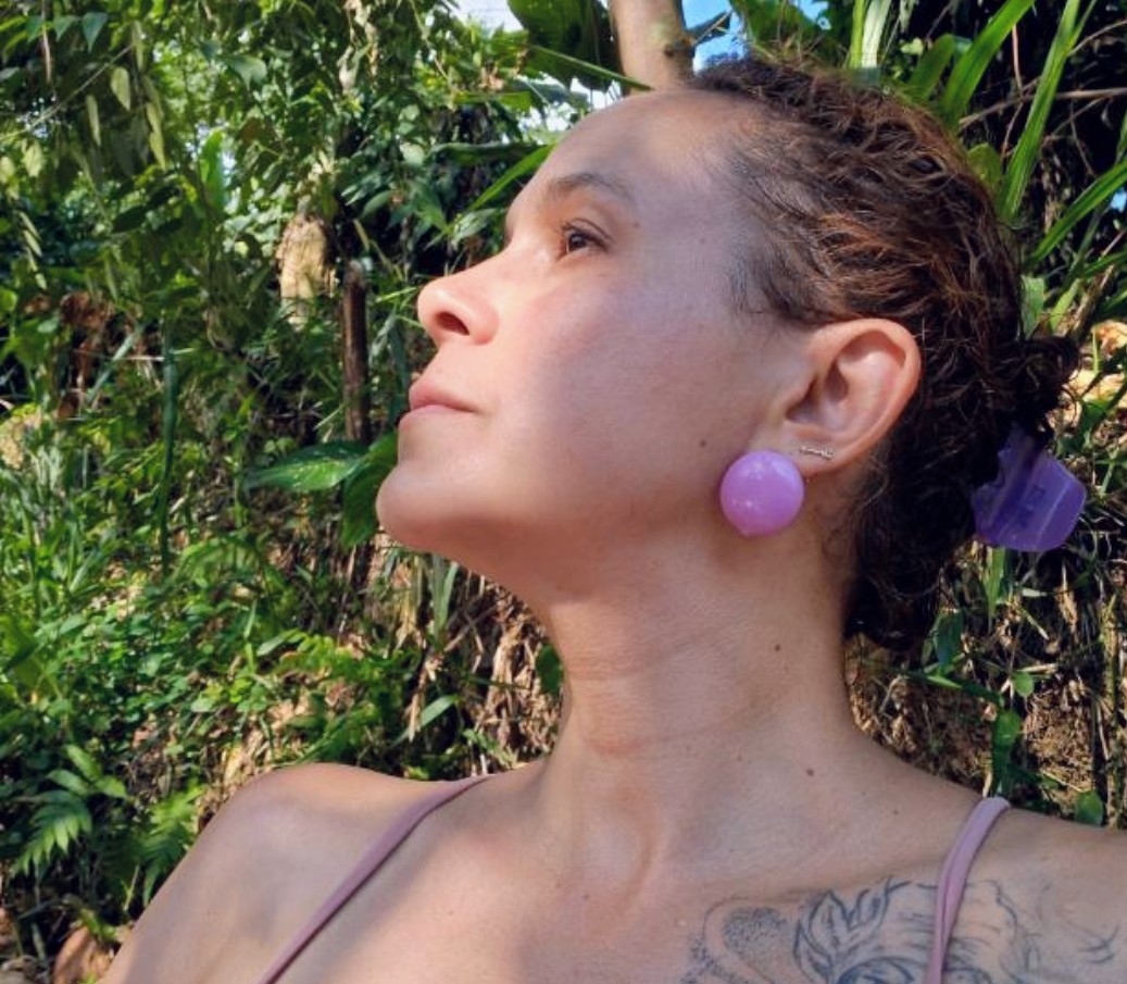 Karen de perfil, banhada pelo sol entre folhagens